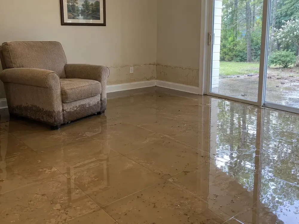 Brown water across a family room floor, with muddy wall marks and a soaked armchair