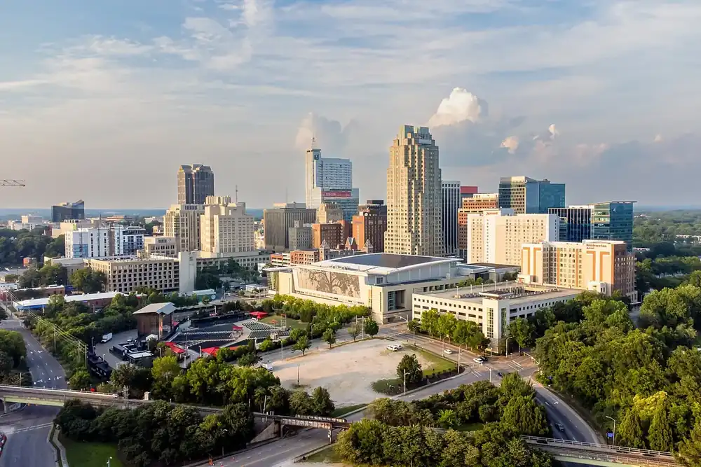 Downtown Raleigh skyline and convention center above green trees, seen from Dorothea Dix Park
